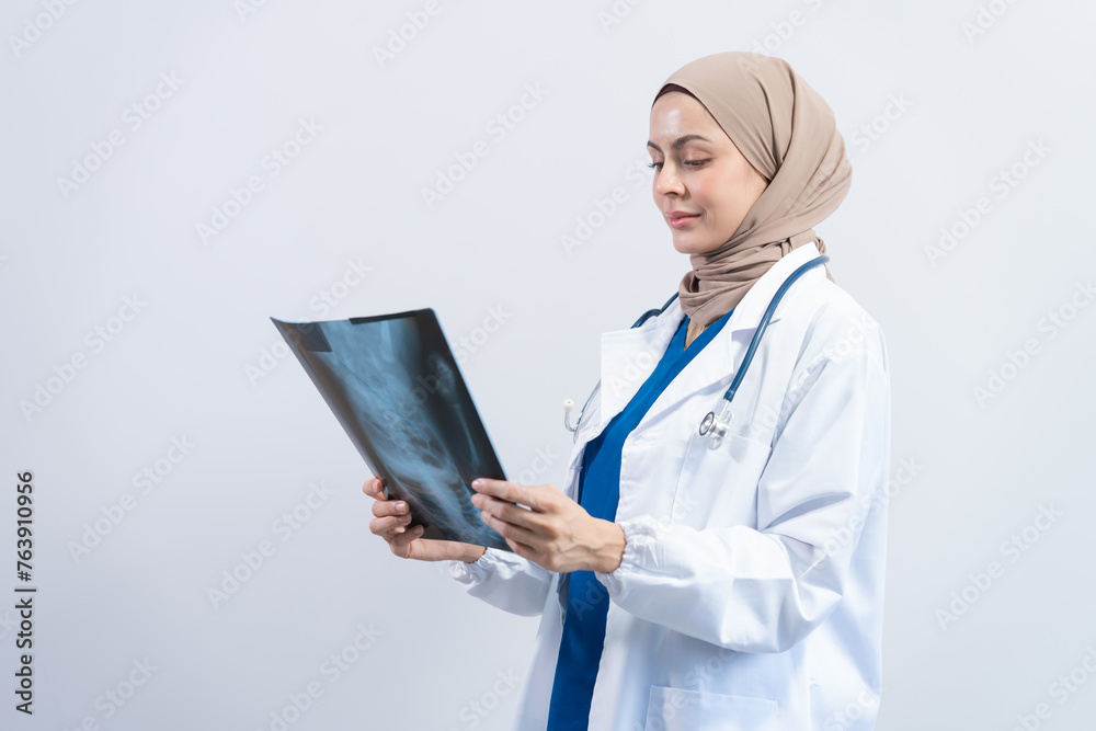 Asian Muslim doctor in hijab and scrubs headphones around her neck Stand confidently in the medical office, isolated on white background, holding x-ray film. Asian Muslim doctor in hijab and scrubs headphones around her neck Stand confidently in the medical office, isolated on white background, holding x-ray film.