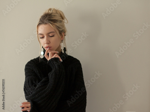 Beautiful young girl wearing warm black sweater and fashion jewellery over pastel background