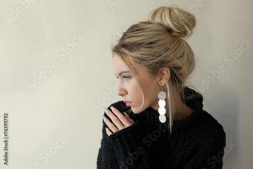 Beautiful young girl wearing warm black sweater and fashion jewellery over pastel background