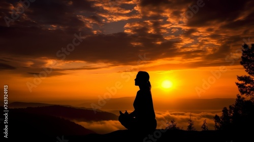 A tranquil silhouette of an individual meditating atop a hill as the sun rises, casting a warm glow over a mist-covered valley.