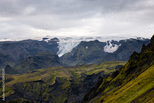 The picturesque view along a famous Laugavegur hiking trail. Amazing Icelandic landscape of volcanic mountains and glacier in cloudy weather with green grass and moss. Iceland in august.