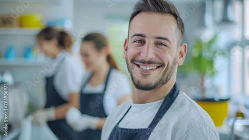 A smiling chef in a bustling kitchen with colleagues working in the background.