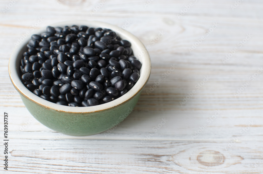 Raw black bens in a green bowl on a white wooden background. Concept of healthy eating. Vegetarian and vegan food. Horizontal orientation. Selective focus. Copy space Raw black bens in a green bowl on a white wooden background. Concept of healthy eating. Vegetarian and vegan food. Horizontal orientation. Selective focus. Copy space