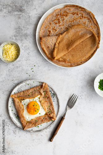 Homemade buckwheat crepes. Galettes Bretonnes with cheese and fried egg on a grey background. Traditional French cuisine.