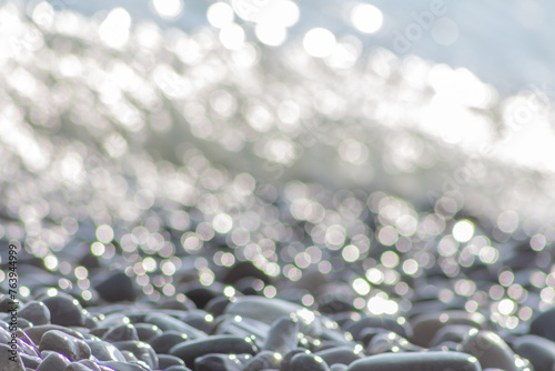 Pebble stones on sea shore close up in defocused bokeh lights. Grey pebble stones background, soft focus.