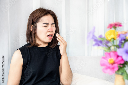 allergic Asian woman suffer from pollen allergy symptoms sneezing and has runny nose with bloom flower in living room