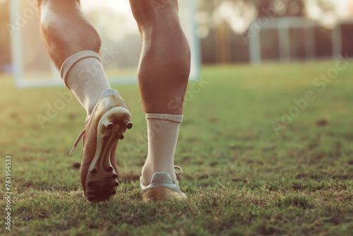 Closeup of soccer player walking on grass field. Legs of footballer playing competition match. Sports horiznotal background. Athlete in soccer cleats and soccer socks