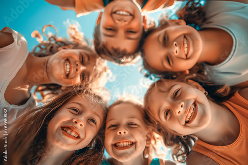 Bunch of cheerful joyful cute little children playing together and having fun. Group portrait of happy kids huddling, looking down at camera and smiling. Low angle, view from below. Friendship concept photo