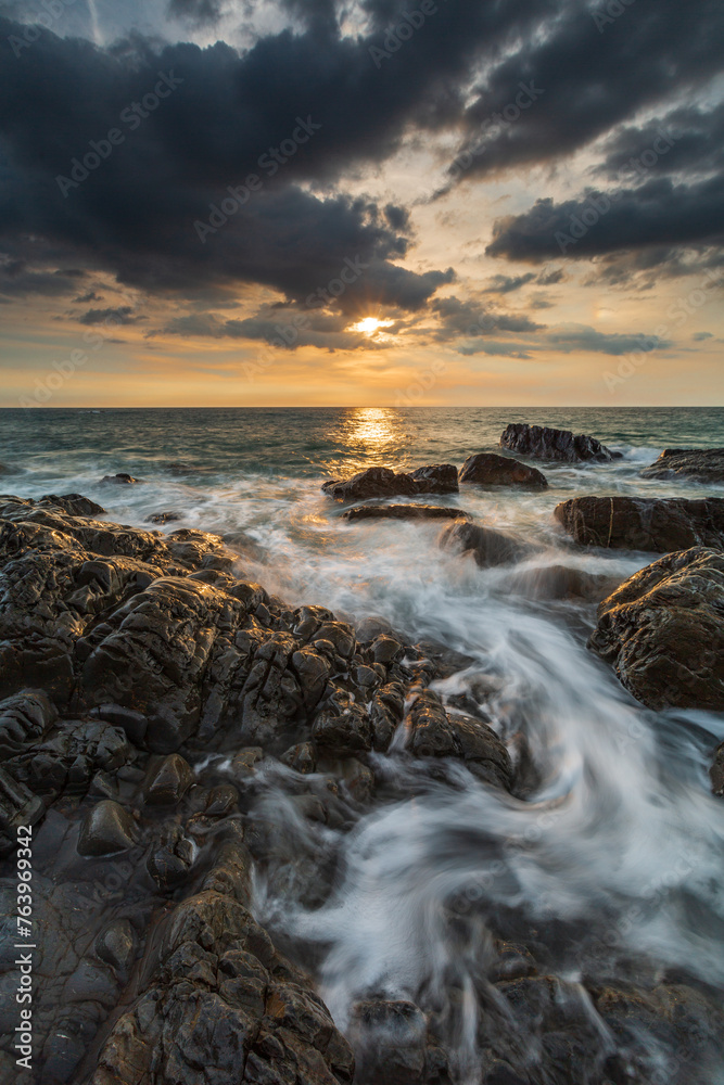 Vertical of the sea against the rocky shore at sunset