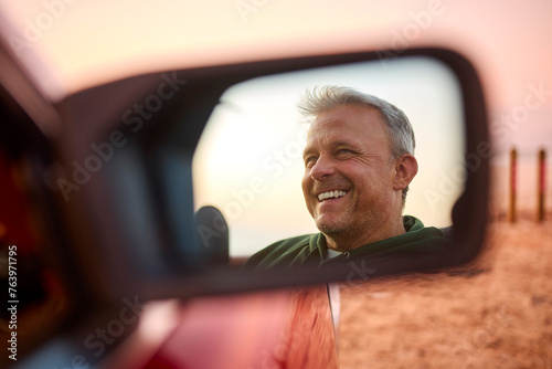 Retired Senior Man Reflected In Mirror Of Classic Open Top Sports Car At Beach Watching Sunrise photo