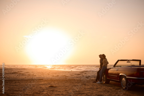 Retired Senior Couple On Vacation Standing By Classic Sports Car At Beach Watching Sunrise