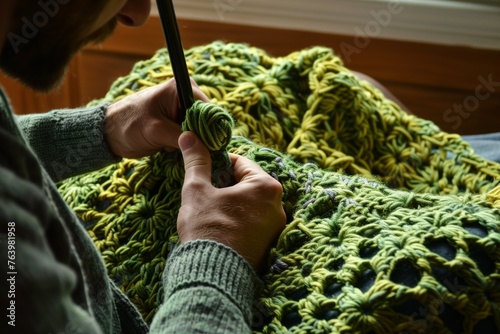man crocheting a green blanket with a large hook photo