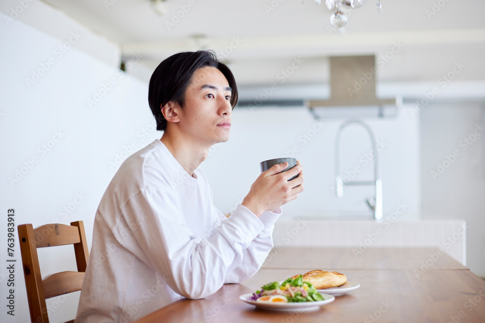 リビングにて朝食を食べる若い日本人の男性