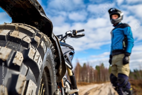 rider standing next to a bike, focus on dual sport tire tread photo