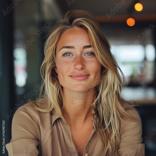 A woman with blonde hair and a tan shirt is smiling at the camera