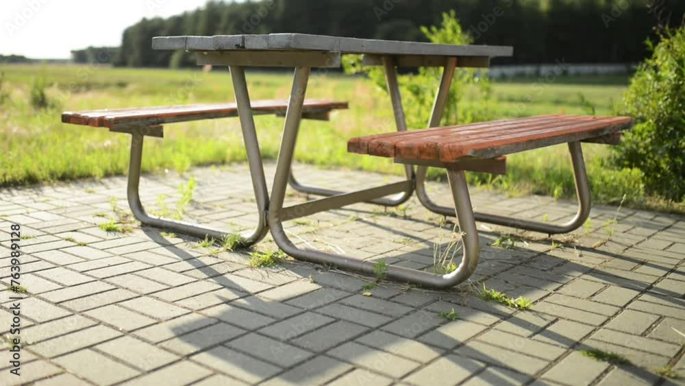 Wooden bench and table on a metal basis against the background of the summer field. Forest in the background. Wooden bench and table on a metal basis against the background of the summer field. Forest in the background.
