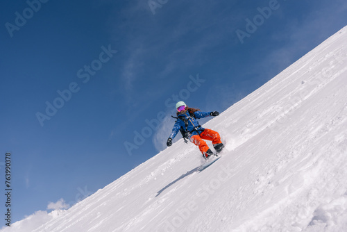 female snowboarder riding on slope of powdery snow in high mountains. Freeride at ski resort, amazing mountain peaks skyline