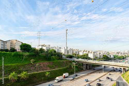 Car and truck traffic on an important avenue in the city of Belo Horizonte. Buildings, bridge and highway. Blue sky with clouds. Trees. Power poles. Horizontal.
