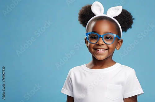 funny happy afrian american girl wearing bunny headband and glasses, on solid pastel blue background. Easter holiday concept. Easter ophtalmological concept photo