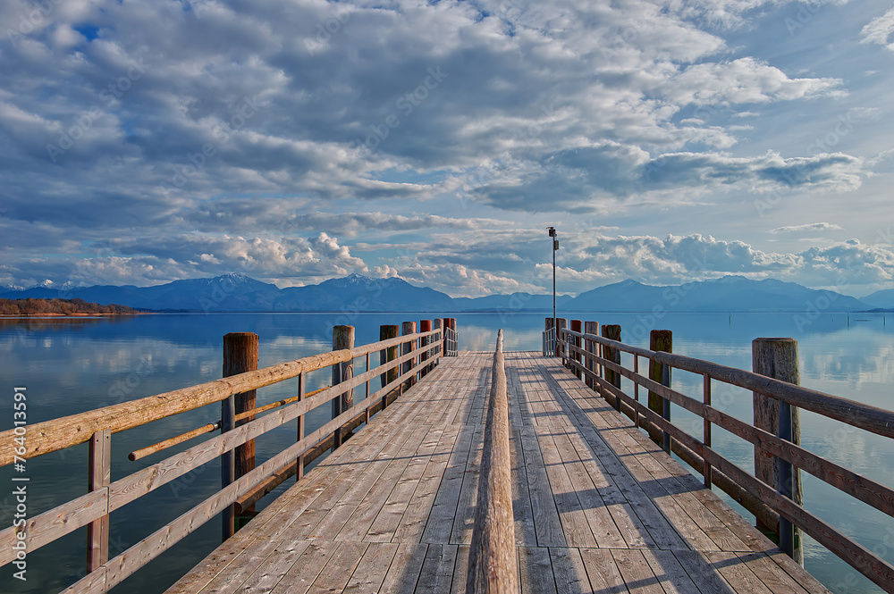 Scenic of a wooden stage at the lake agains the cloudy blue sky and the high mountains