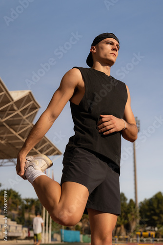 Young male athlete warming up his legs and stretching. Preparing for competition in a sports facility. Vertical photo