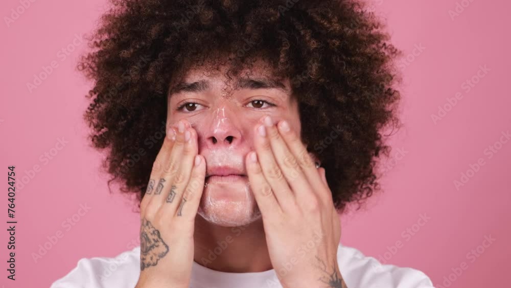 Close-up of a young man with a fluffy afro applying facial cleanser Close-up of a young man with a fluffy afro applying facial cleanser