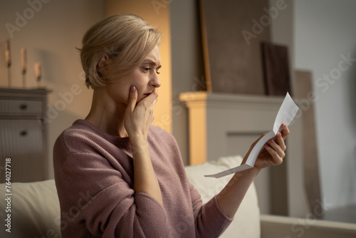 Fotografie A concerned elderly woman is seated, holding a letter in her hand, with a look of distress apparent on her face