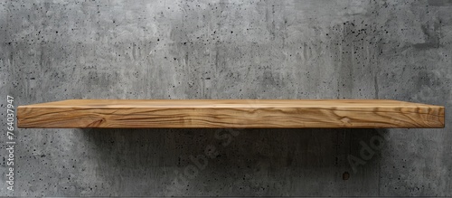 A rectangle wooden shelf made of hardwood is attached to a concrete wall. The wood stain highlights the natural material, creating a beautiful pattern against the grass flooring