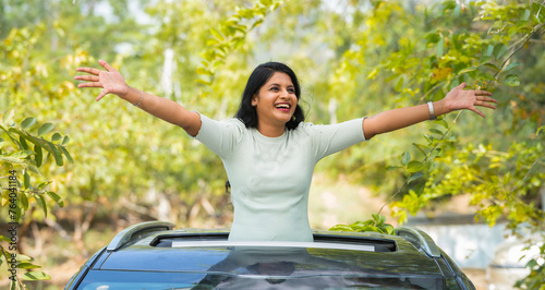 Happy woman feeling nature fresh air by stretching arms on car sunroof - concept of freedom, traveller and refreshment