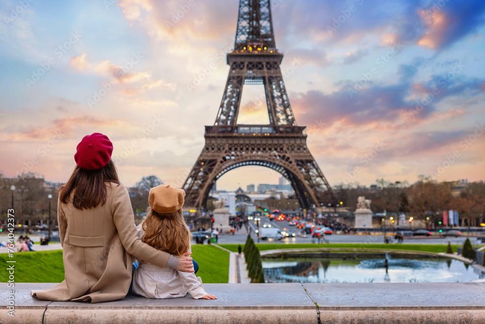 Family city travel concept with a mother and her daughter looking at the beautiful sunset view of the Eiffel Tower in Paris, France - obrazy, fototapety, plakaty 