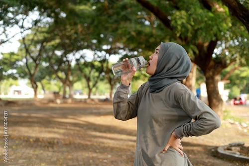 Asian sport muslim woman drinking mineral water from her transparent plastic bottle