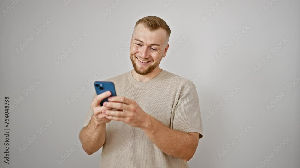 Handsome young man with beard smiling while using smartphone against white wall. Handsome young man with beard smiling while using smartphone against white wall.