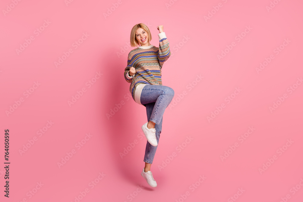 Full length photo of optimistic lovely woman dressed print sweater jumping win lottery shout yeah isolated on pink color background Full length photo of optimistic lovely woman dressed print sweater jumping win lottery shout yeah isolated on pink color background
