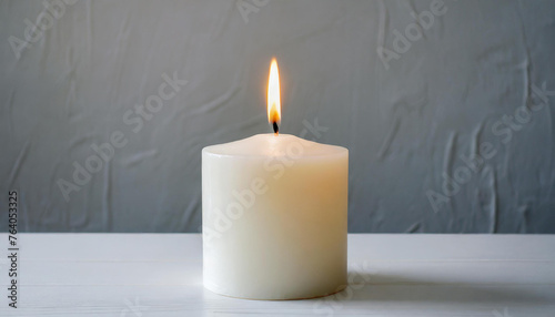 White burning candle white table. Gray backdrop.