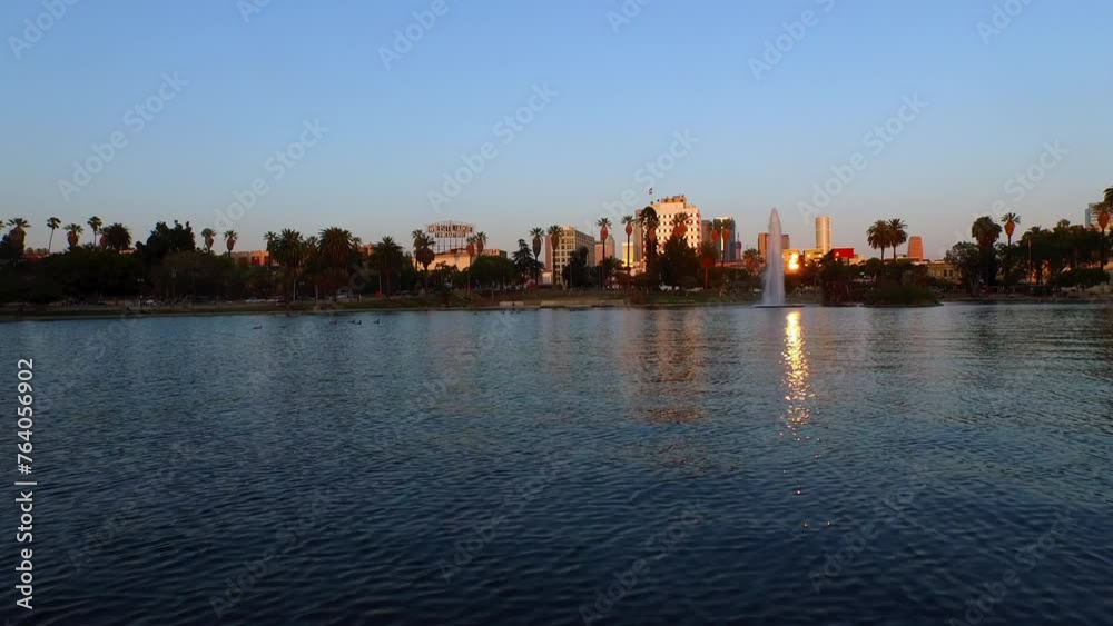 Aerial: Scenic View Of Buildings Against Clear Sky, Drone Flying Forward Over Rippled Lake At Sunset - Los Angeles, California