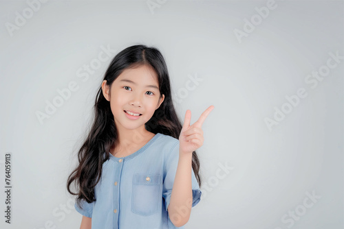 Young and cute Asian girl with long black hair pointing up hands to copyspace on gray background 