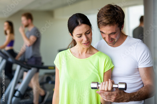 Handsome man personal trainer helping fit woman working with dumbbells in fitness gym club