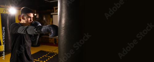 Boxer in gloves impacts on punching bag in dark gym, have hard training. Sports concept. copy space.