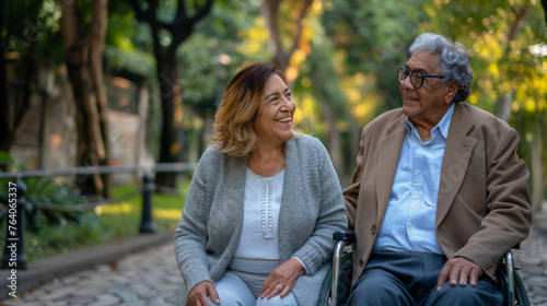 A smiling couple enjoys a moment together in a park, with one seated in a wheelchair.