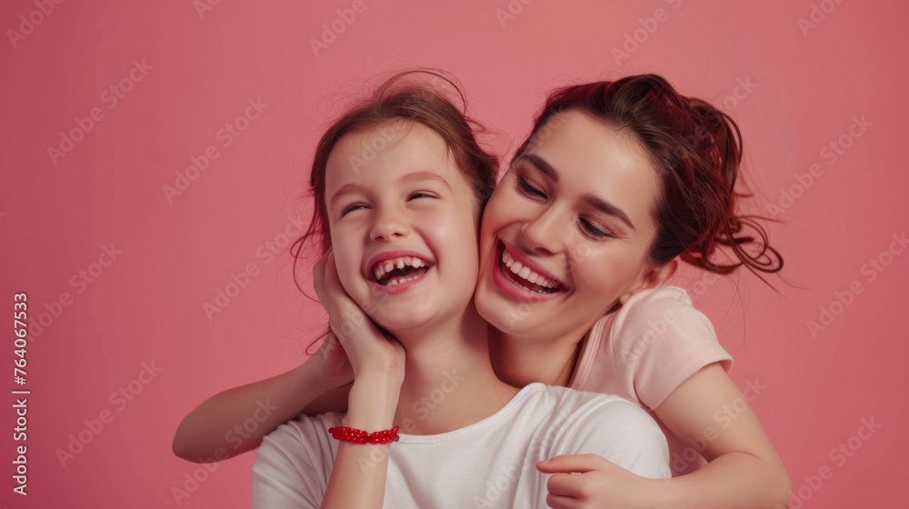 A smiling woman and a laughing young girl are embracing against a pink background. A smiling woman and a laughing young girl are embracing against a pink background.