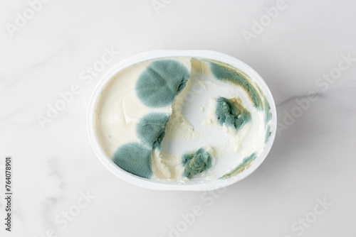 Spoiled cream cheese. Cream cheese packaging with green mold. Food waste.