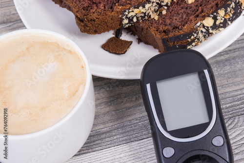 Glucose meter, sweet chocolate cake and cup of coffee with milk. Checking sugar level during diabetes