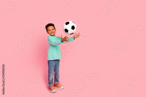 Full length photo of adorable little boy catch soccer ball dressed stylish cyan garment isolated on pink color background © deagreez