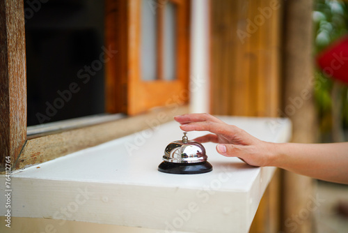 A customer's hand is ringing bell which is placed on the counter at the coffee or restaurant cafe. Action for business concept scene. Close-up and selective focus.