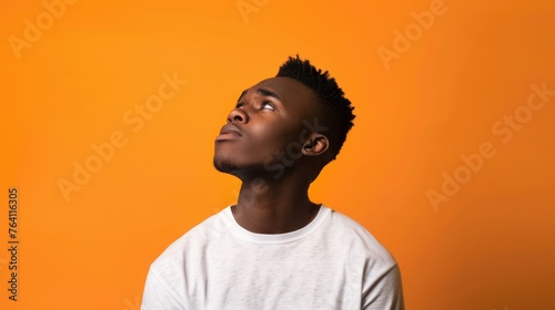 Contemplative young man with a thoughtful expression, looking upward in curiosity against a warm orange backdrop - AI generated.