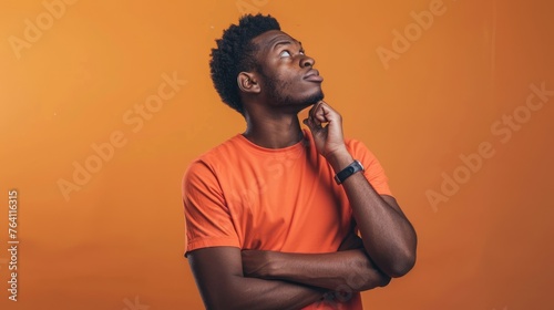 Contemplative young man with a thoughtful expression, looking upward in curiosity against a warm orange backdrop - AI generated.