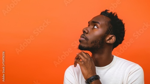 Contemplative young man with a thoughtful expression, looking upward in curiosity against a warm orange backdrop - AI generated.