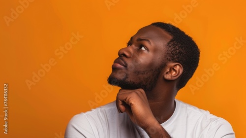 Contemplative young man with a thoughtful expression, looking upward in curiosity against a warm orange backdrop - AI generated.