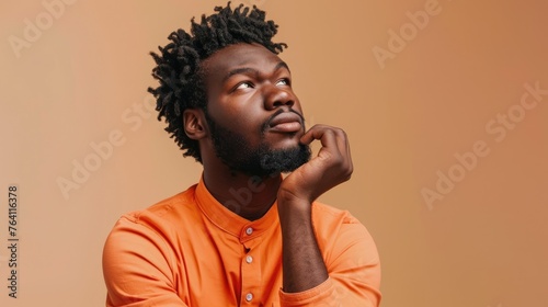 Contemplative young man with a thoughtful expression, looking upward in curiosity against a warm orange backdrop - AI generated.