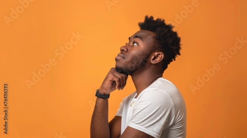 Contemplative young man with a thoughtful expression, looking upward in curiosity against a warm orange backdrop - AI generated.